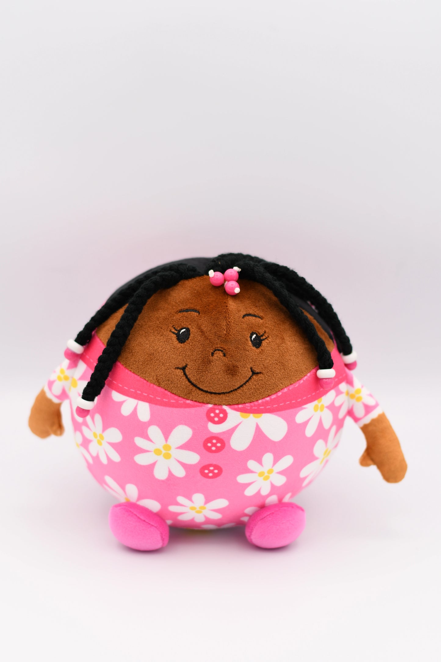 Plush toy with a smiling face, black hair, and pink dress with white flowers on a white background