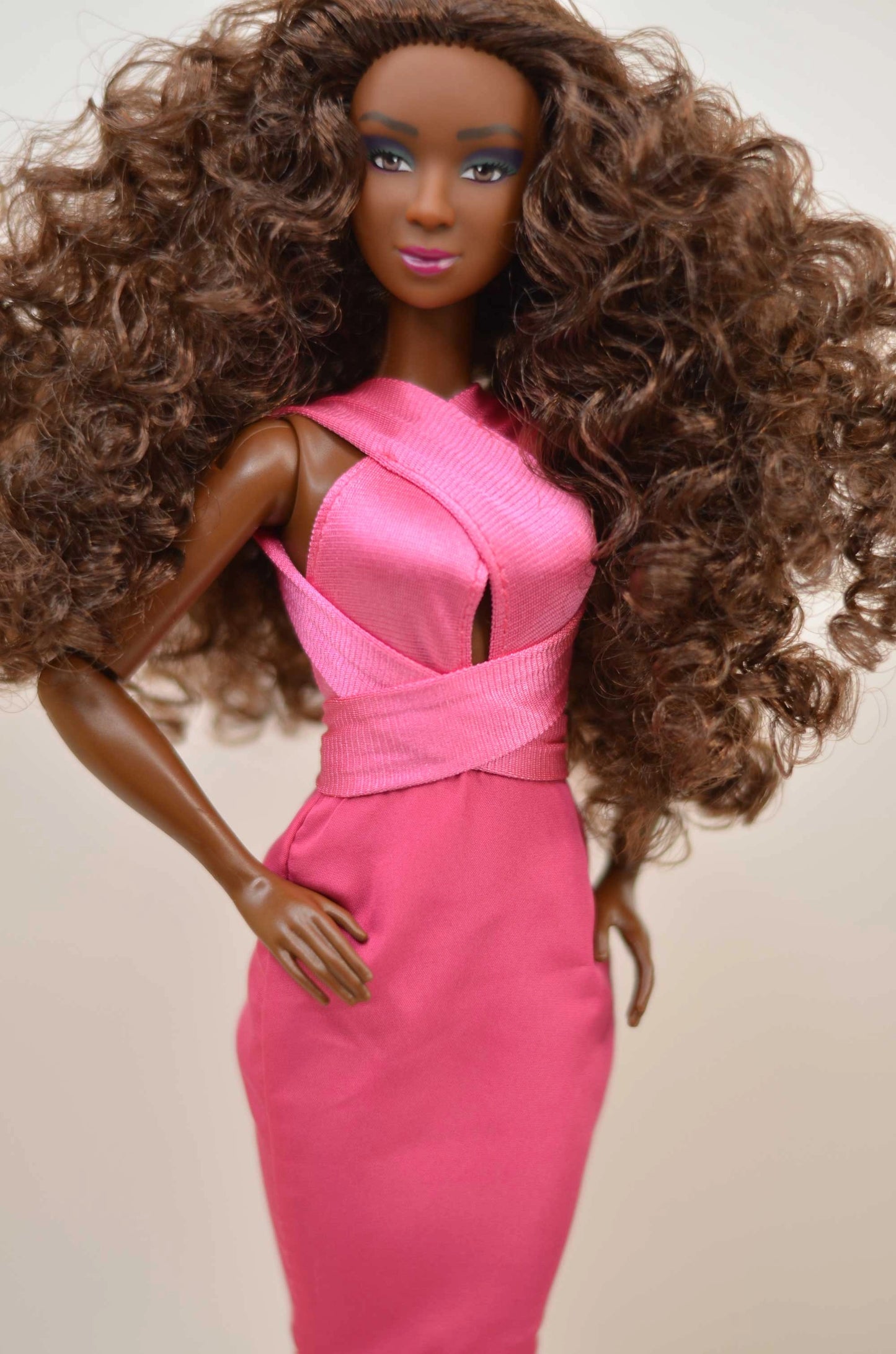Barbie doll with long brown hair wearing a pink dress on a beige background