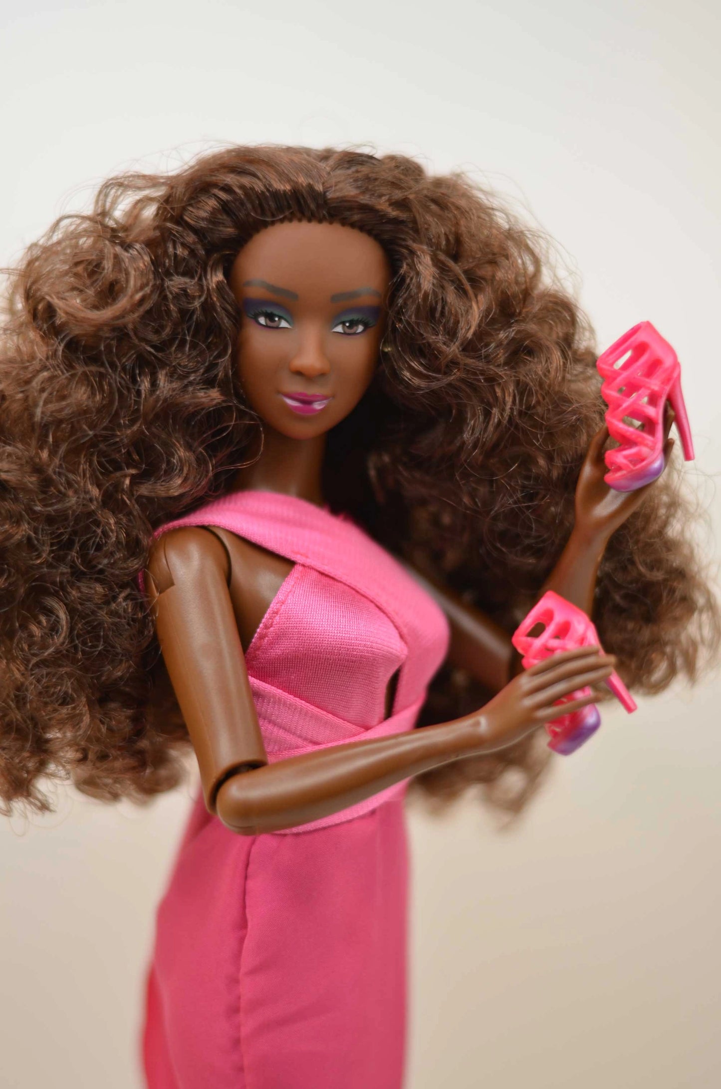 Barbie doll with long curly hair wearing a pink dress and high heels on a plain background