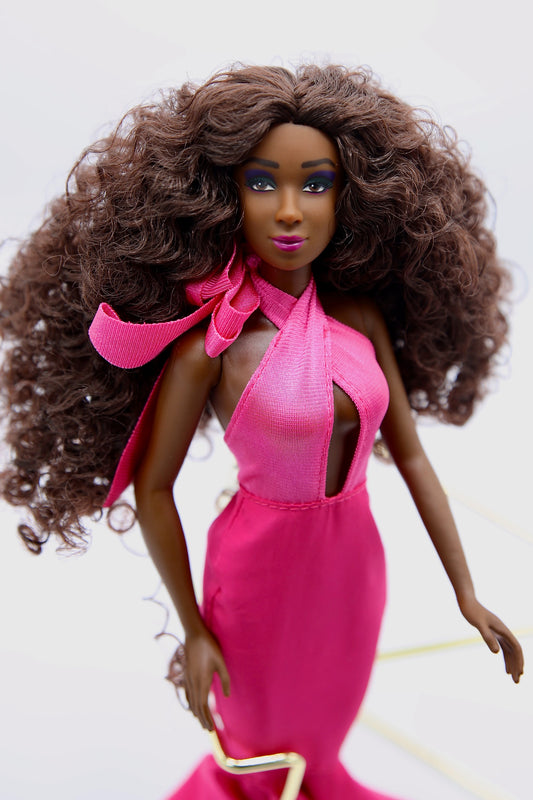 Doll with long curly hair wearing a bright pink dress on a white background