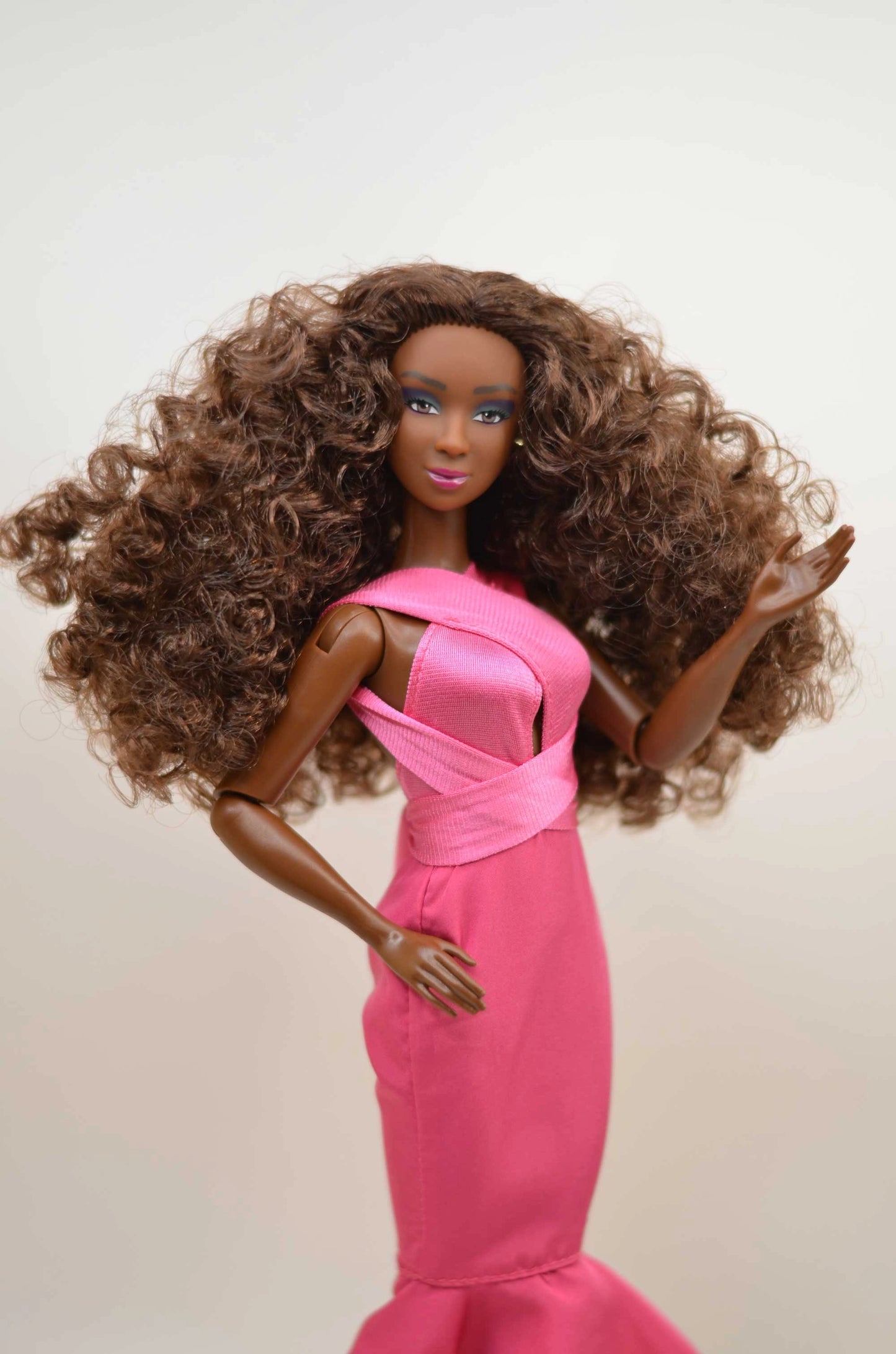 Barbie doll with long curly hair wearing a pink dress on a plain background