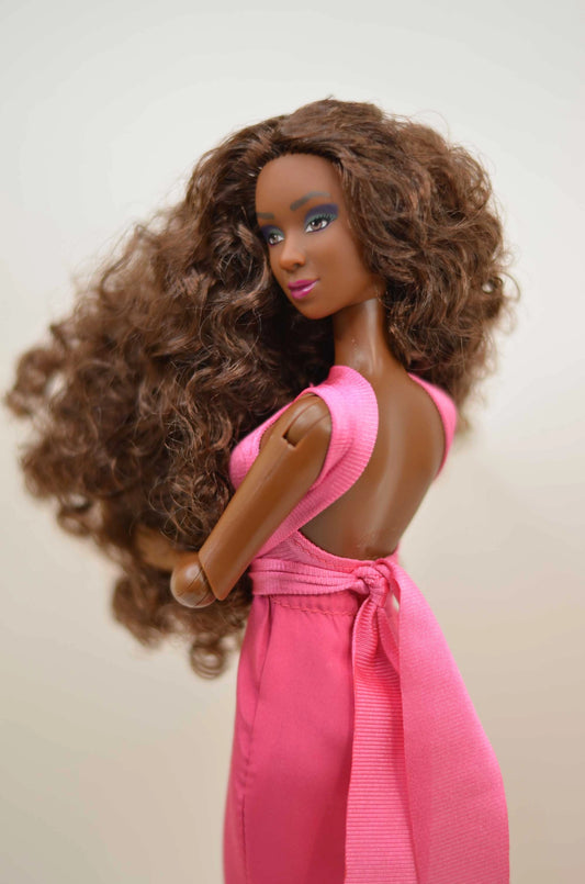 Barbie doll with curly hair wearing a pink dress on a plain background