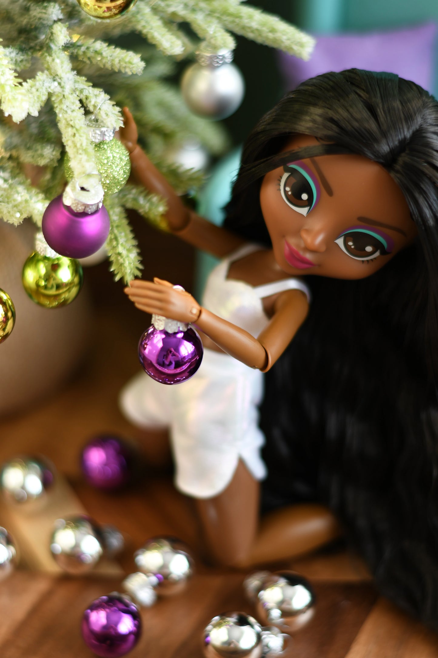 Doll holding a purple ornament near a decorated Christmas tree