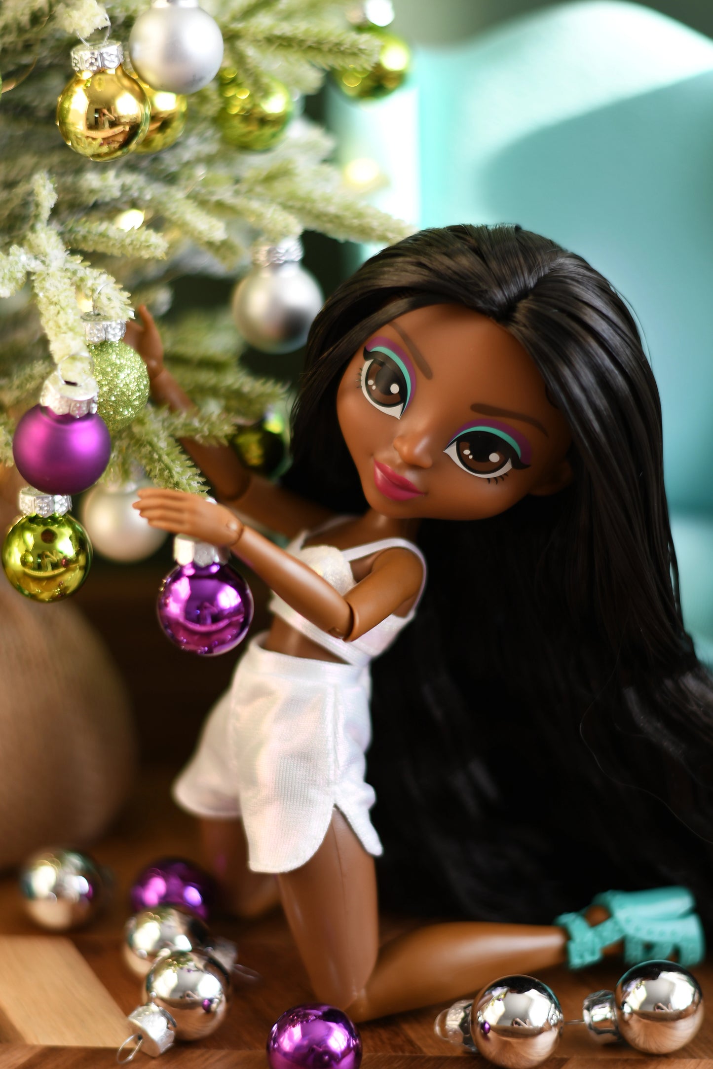 Doll with long dark hair and white outfit near a Christmas tree with ornaments
