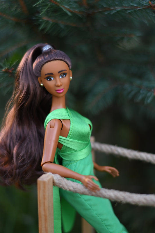 Barbie doll in a green dress hanging from a rope with a blurred natural background