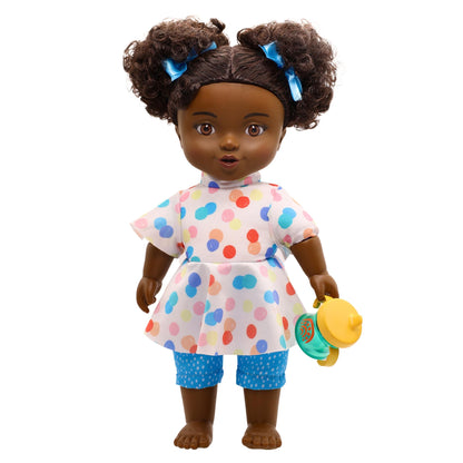 A toddler doll with curly hair, wearing a multicolored dress and polka dot pants, holding a rattle.