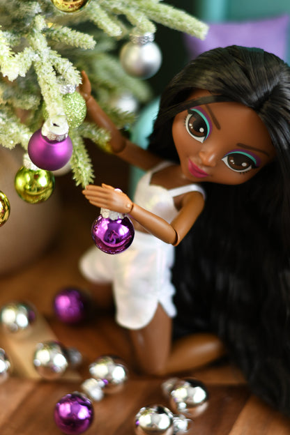 Doll holding a purple ornament near a decorated Christmas tree