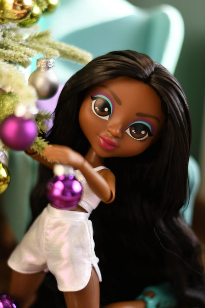 Doll with long dark hair holding a purple ornament in front of a Christmas tree.