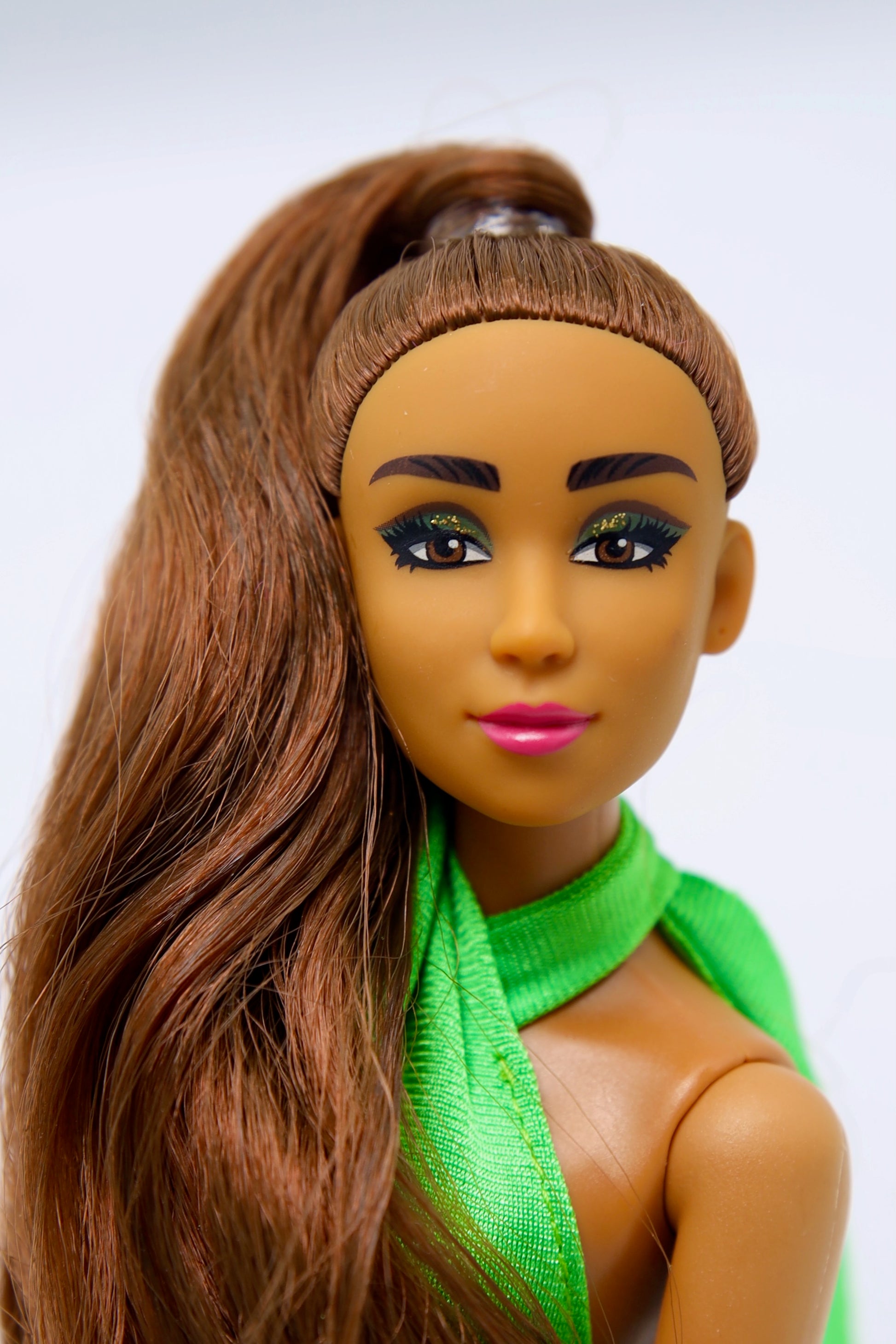 Barbie doll with brown hair and green top on a white background