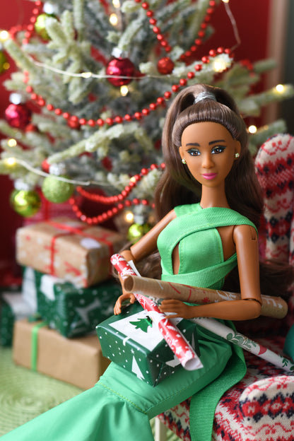 Barbie doll in a green dress lying next to a Christmas tree with presents.