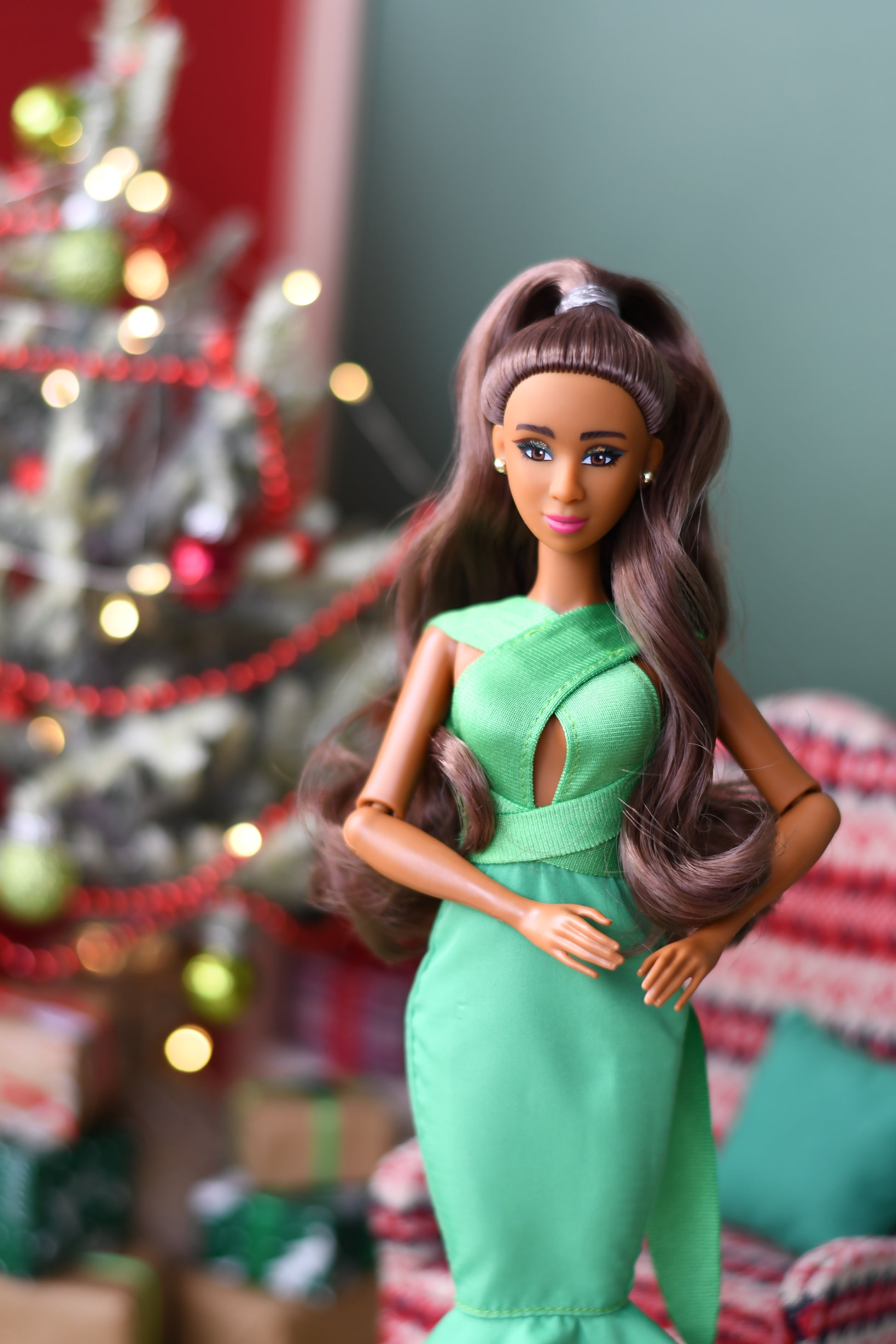 Barbie doll in a green dress lying on a surface with a blurred Christmas tree in the background