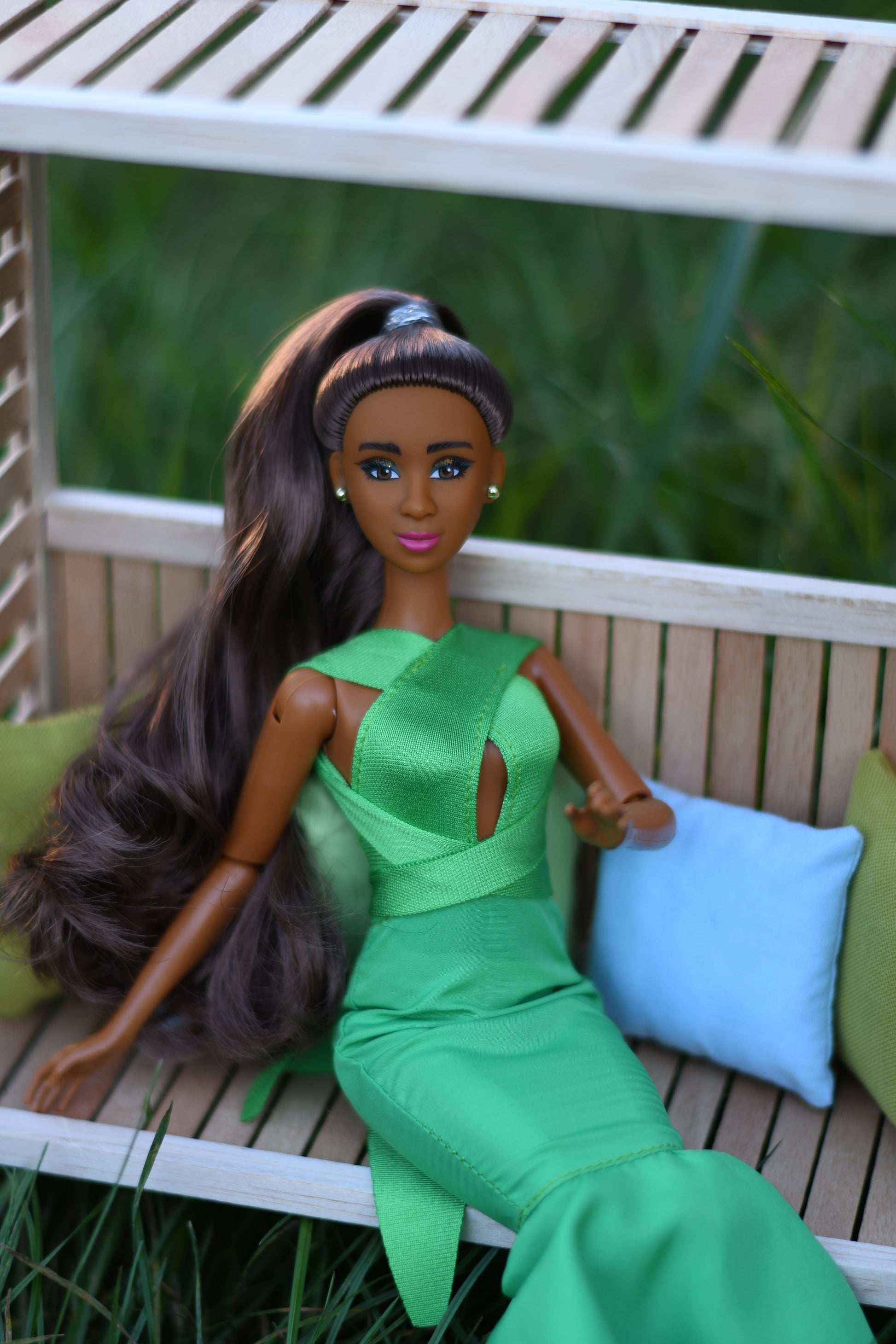 Barbie doll in a green dress sitting on a wooden bench with a blurred grassy background