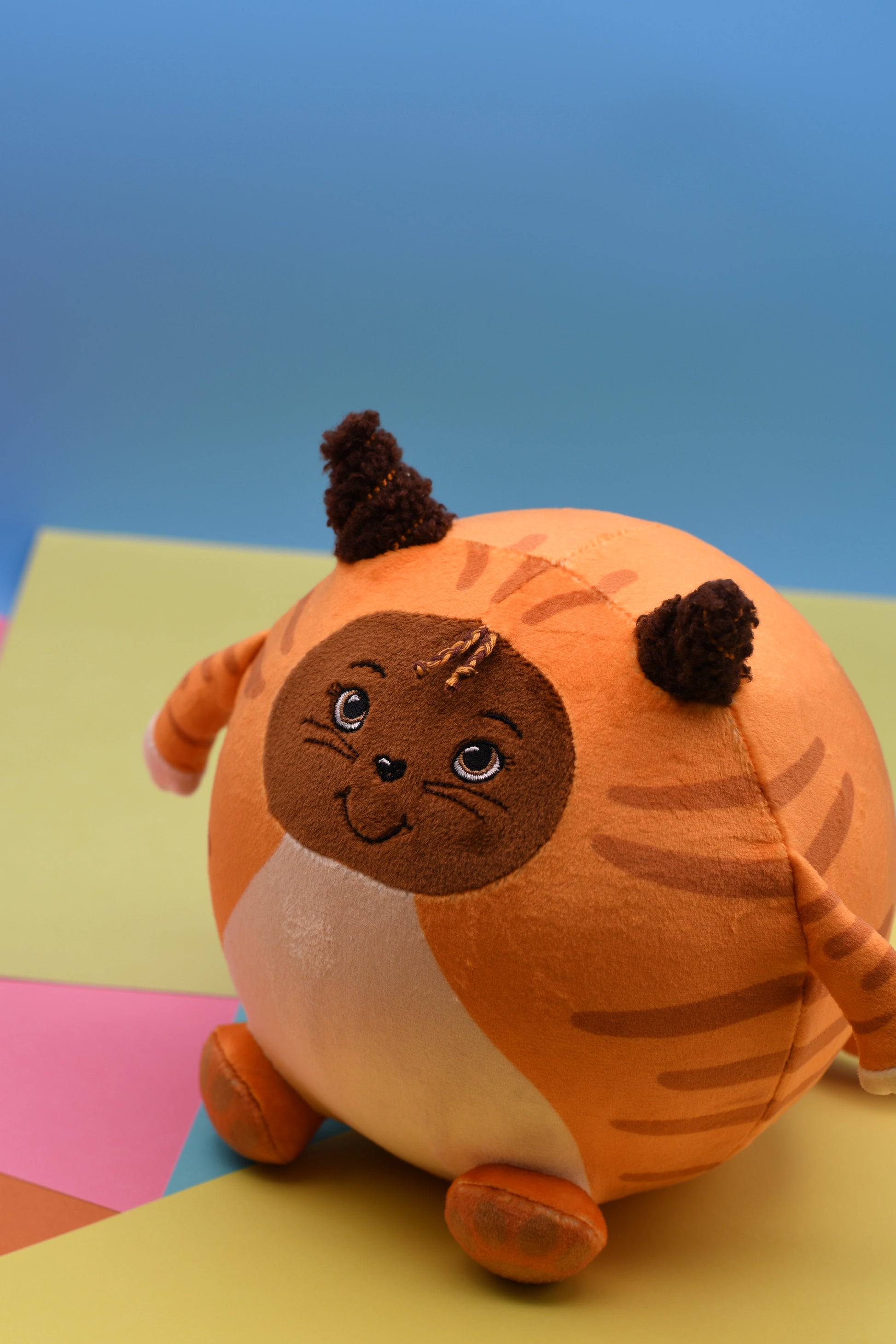 Plush toy resembling a cat with a round body on a colorful background